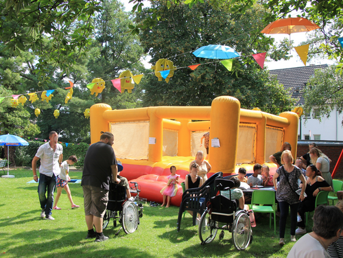 Buntes Treiben im dekorierten Garten: Menschen mit und ohne Beeinträchtigungen feiern gemeinsam bei unserem Sommerfest. Eine Hüpfburg lädt zum Springen ein.