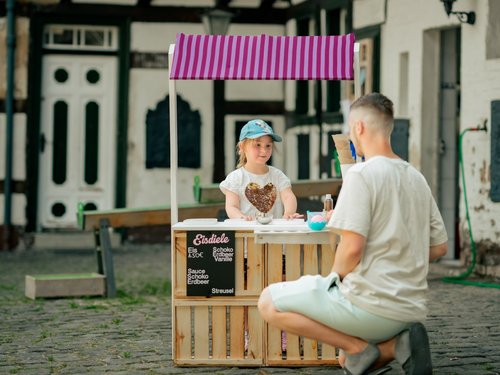 Ein junges Mädchen verkauft einem Papa an einer Spieleeisdiele ein Eis.