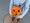 Ein Mädchen in einem grauen Oberteil hält einen kleinen, geschnitzten Halloween-Kürbis mit einem Gesicht in ihren Händen. Sie steht auf einem runden Kanaldeckel im Freien.