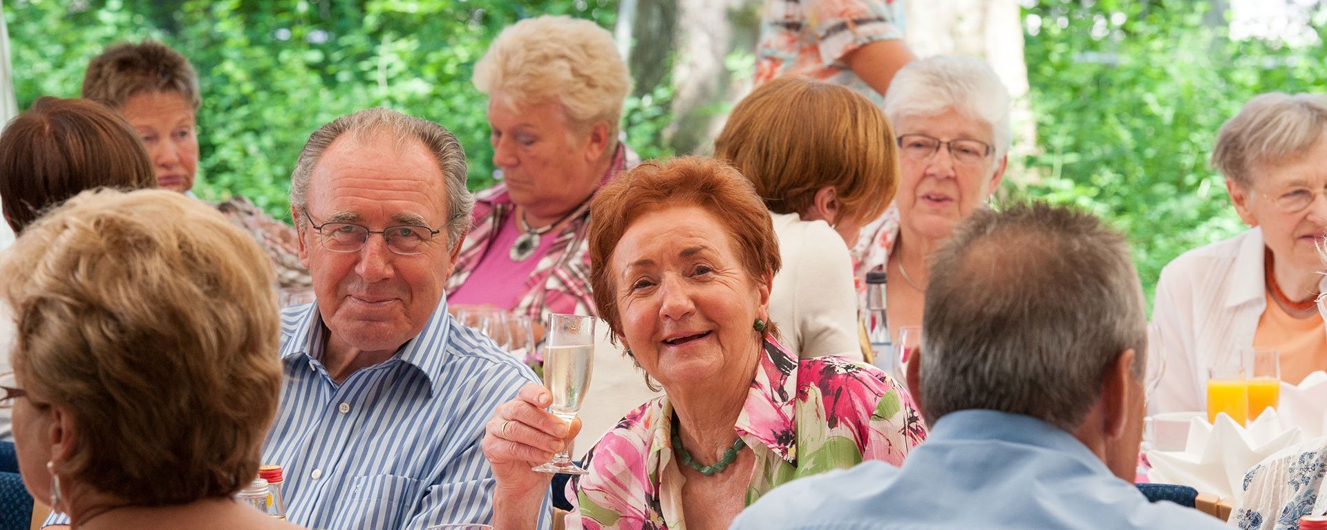 Eine Gruppe an Bewohnern sitzen gemeinsam an einem Tisch und trinken Sekt