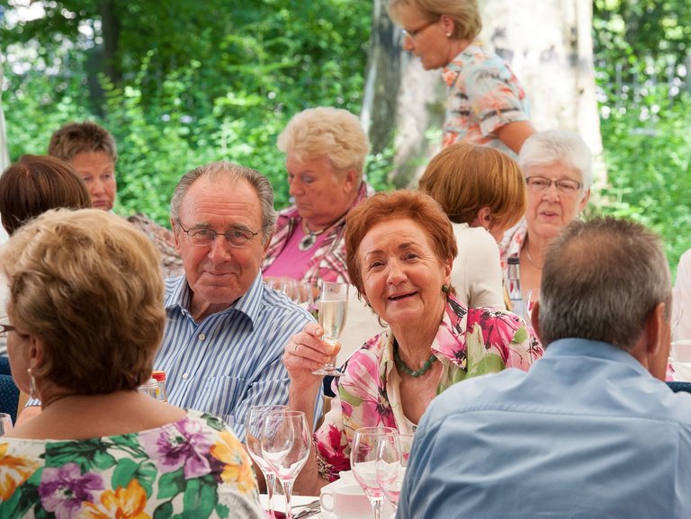 Eine Gruppe an Bewohnern sitzen gemeinsam an einem Tisch und trinken Sekt