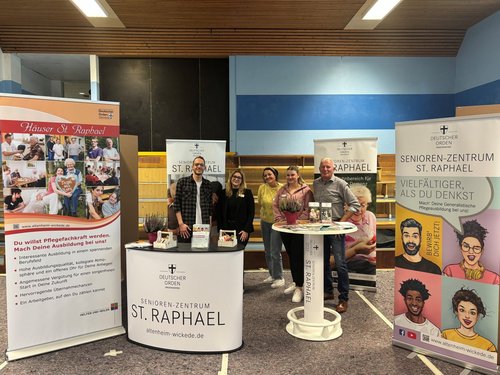 Eine Gruppe Menschen präsentiert das Haus St. Raphael auf einem Messestand.