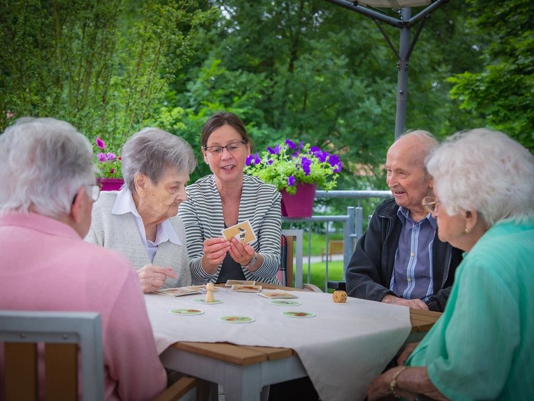 Eine Pflegerin unterstützt Bewohner/innen beim Kartenspiel auf der Terasse