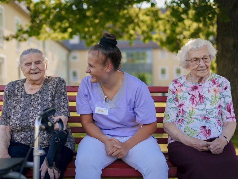 Eine Pflegerin unterstützt Bewohner/innen beim Kartenspiel auf der Terasse