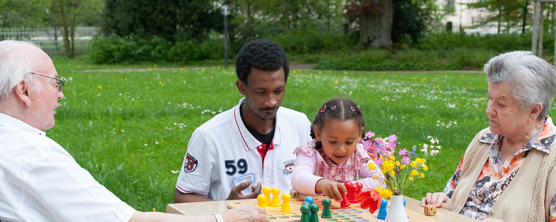 Zwei Bewohner Spielen mit einer Pflegefachkraft und einem kleinen Kind ein Brettspiel