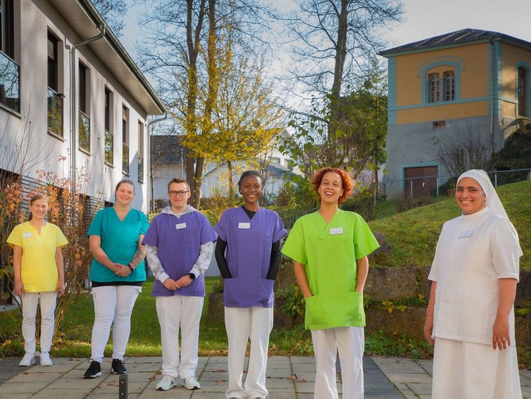 Sechs Mitarbeiter stehen im Garten vor dem Altenheim St. Hildegard und lächeln in die Kamera