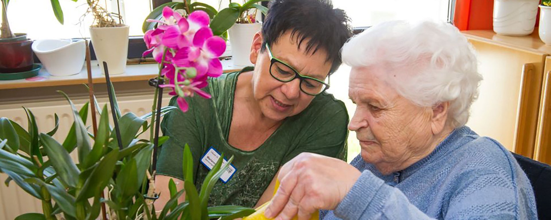 Eine Mitarbeiterin hilft einer Bewohnerin beim gießen ihrer Orchidee.