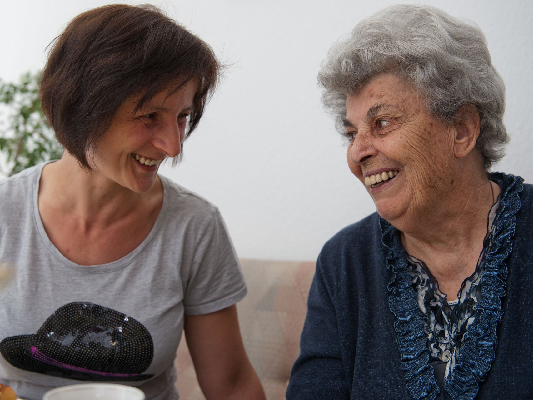 Eine Person unterhält sich mit einer Bewohnerin und sie essen Kuchen