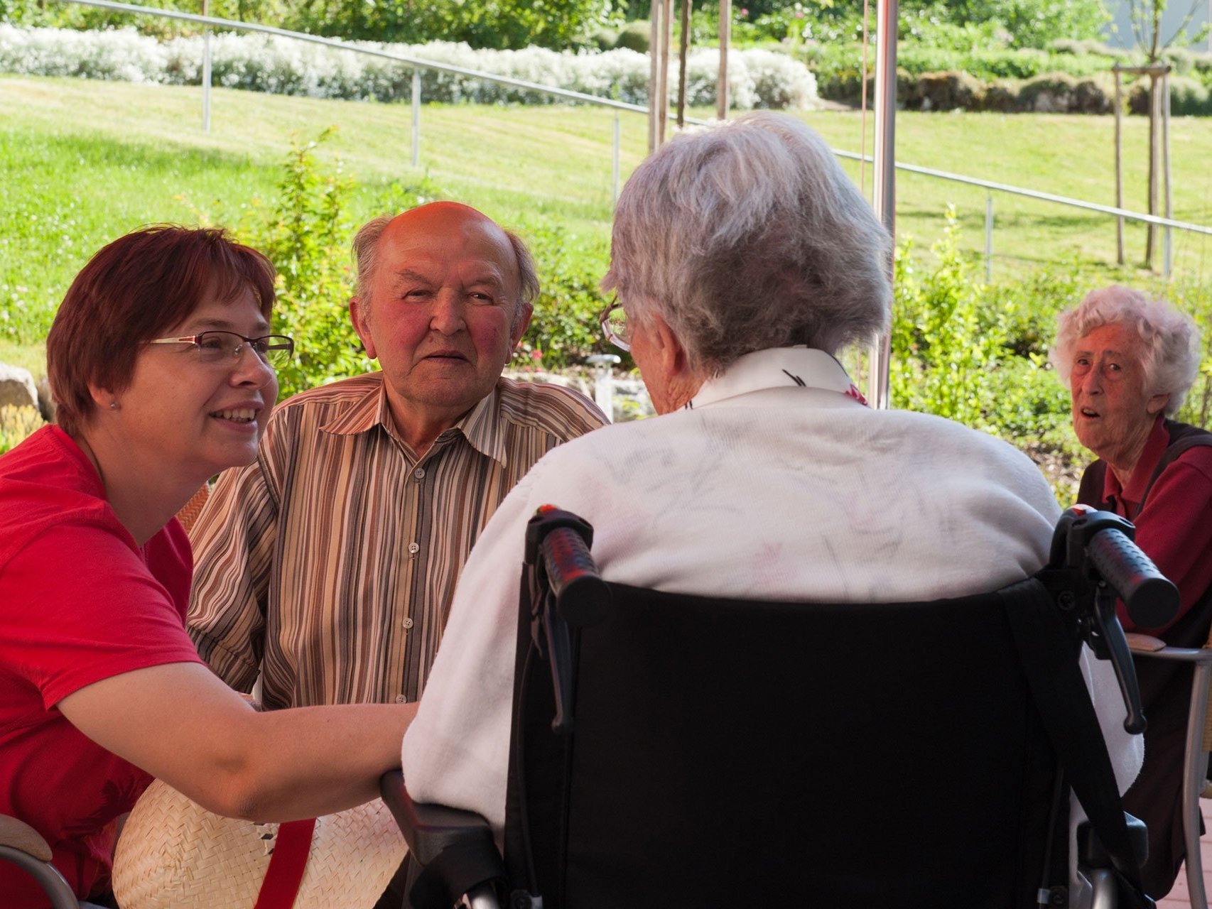 Drei Bewohner sitzen auf der Terrasse und unterhalten sich mit einer Mitarbeiterin