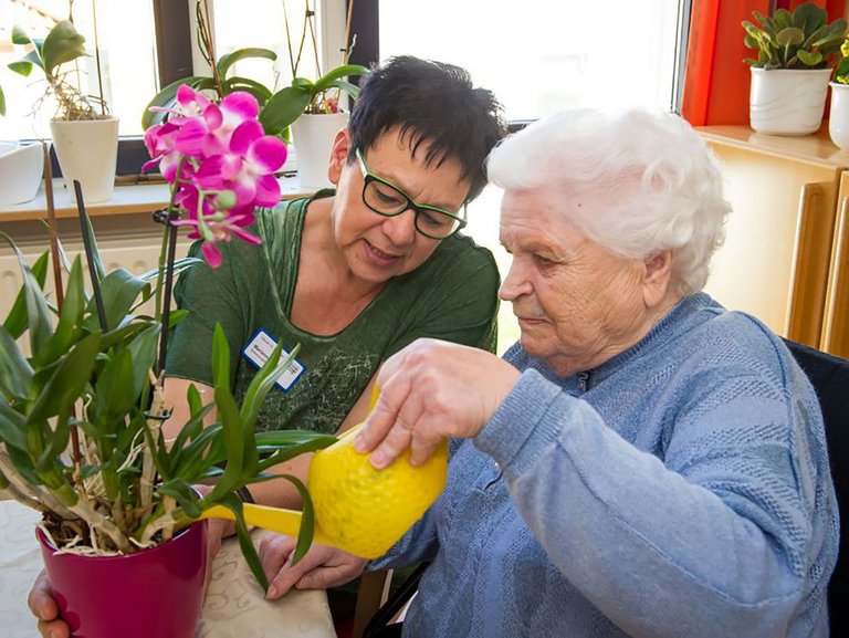 Eine Mitarbeiterin hilft einer Bewohnerin beim gießen ihrer Orchidee.